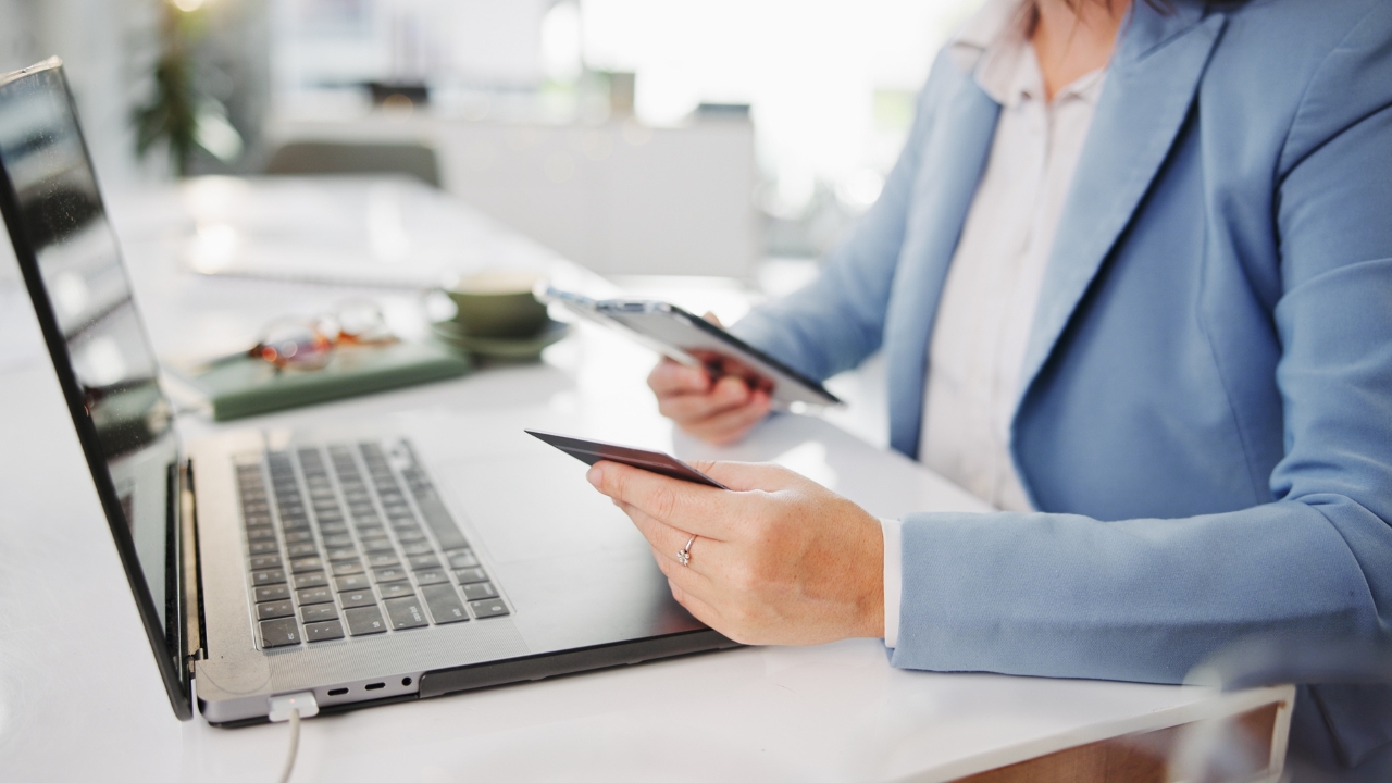 A woman reviews credit cards beside a laptop at a desk