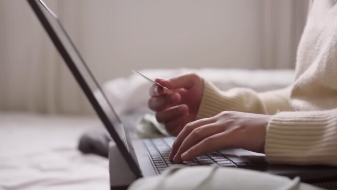 Credit Card Rewards - How to Use Points Without Overspending A person holds a credit card while using a laptop at home