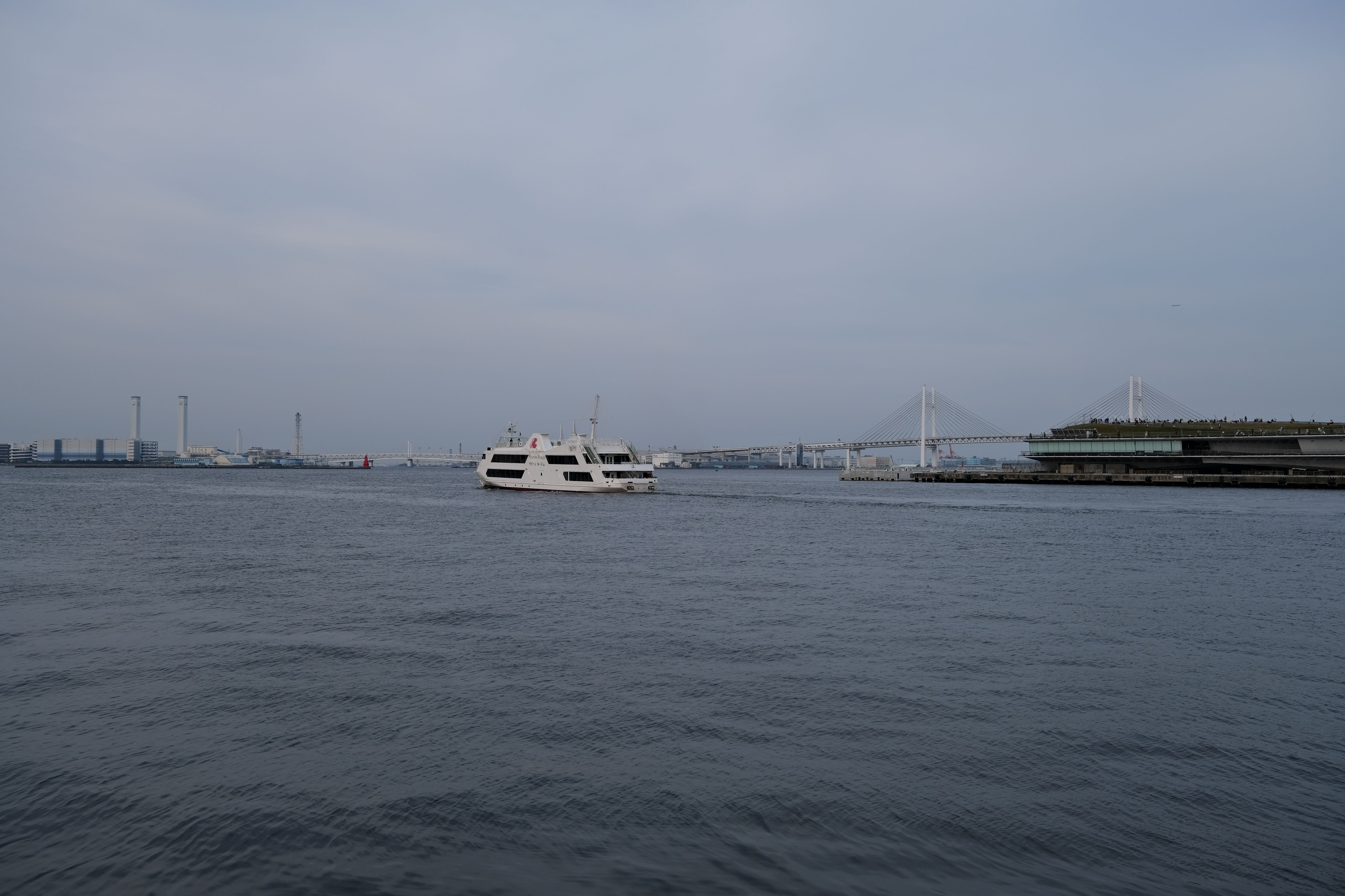 Cruise ship in Yokohama Bay with a Japanese city skyline and bridge behind it.