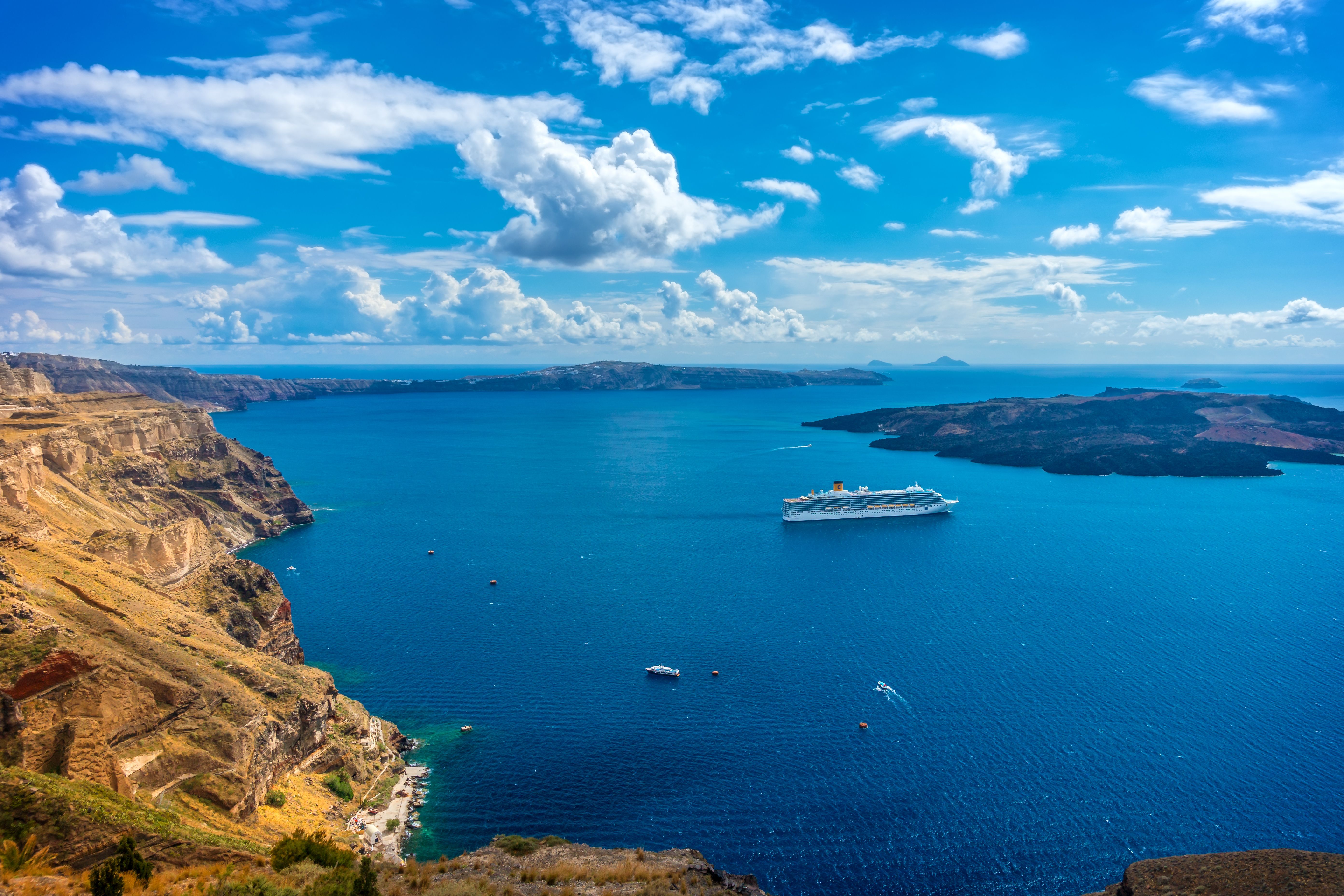 Santorini caldera and whitewashed cliffs viewed from the sea with a cruise ship.