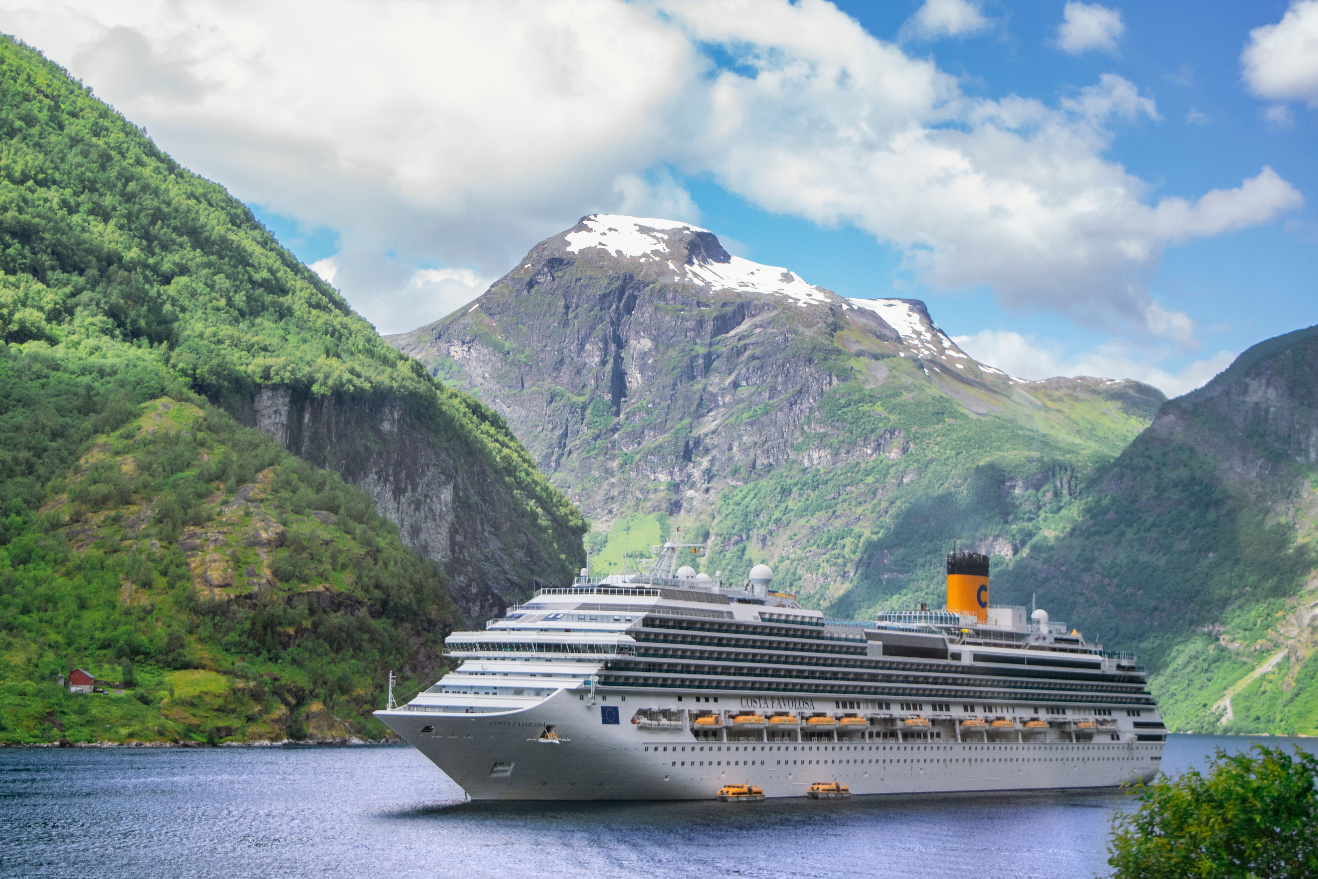 Large cruise ship navigating Norway's Geirangerfjord beneath dramatic mountains.